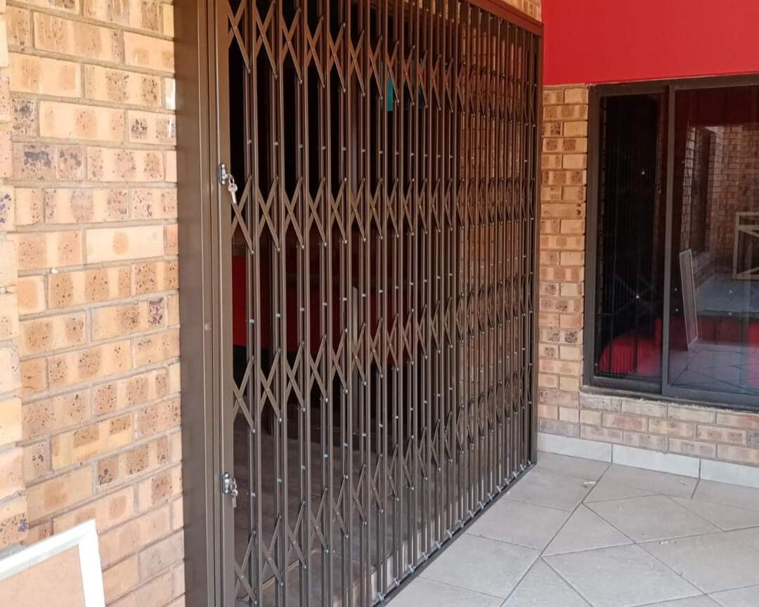 Brown aluminium expanding security gate installed on house with light sand coloured bricks, providing added protection and privacy.